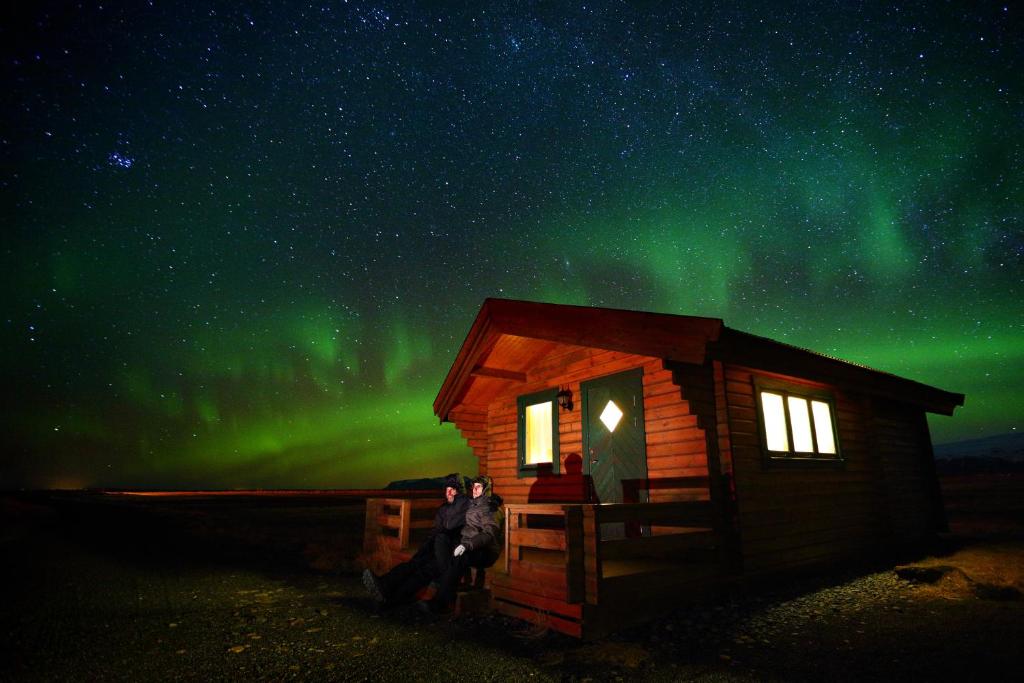 Suður Hvoll米德沃尔小屋旅馆的站在小屋外的北极光下,有两个人