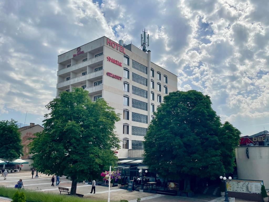 桑丹斯基Spa Hotel Spartak的一座高大的白色建筑,前面有树木
