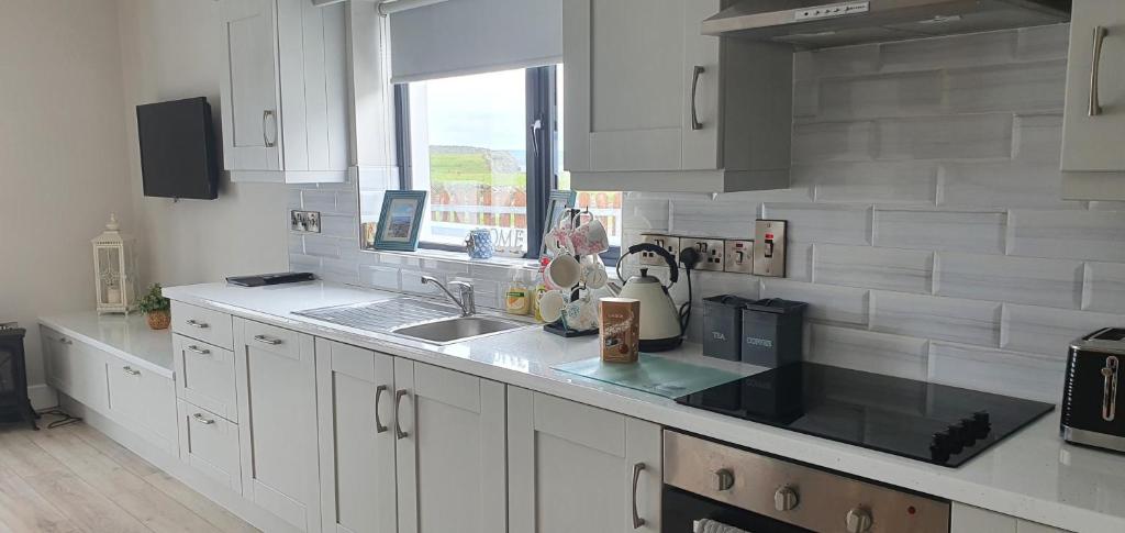 利斯坎诺Beside the sea & minutes from Cliffs-Clahane Shore Lodge的厨房配有白色橱柜、水槽和窗户。