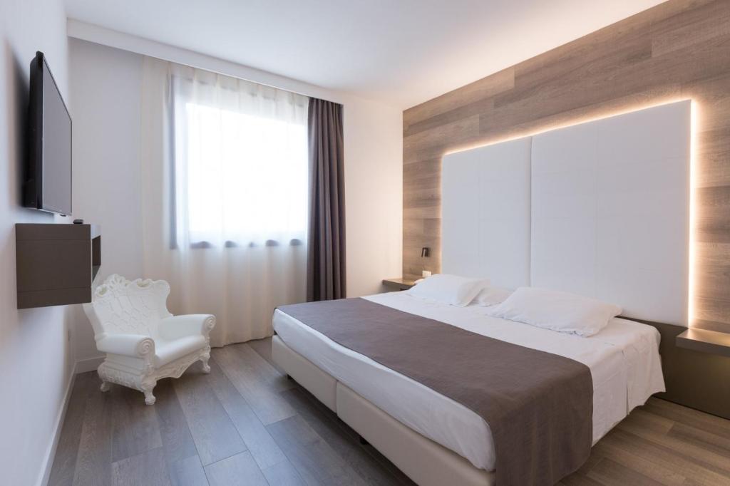 福利尼奥City Hotel & Suites的一间卧室配有一张大床和一张白色椅子