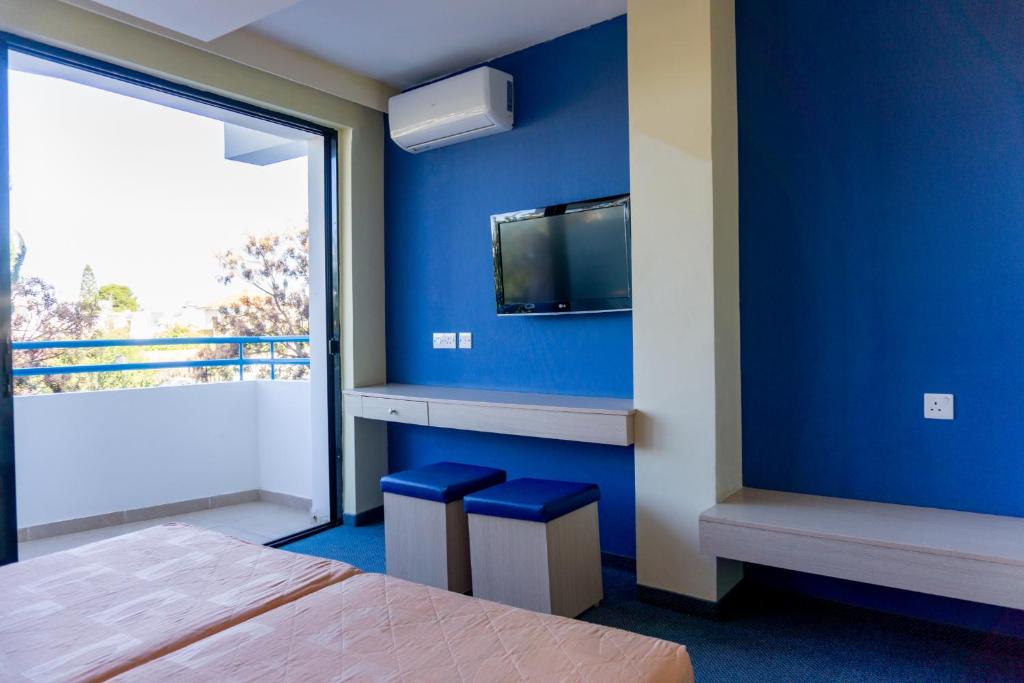 拉纳卡玛丽安第酒店的一间卧室设有蓝色墙壁、电视和凳子