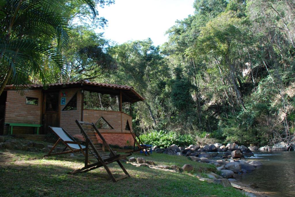 伊塔蒙蒂Pousada Estância Rio Acima的河边带椅子的棚屋
