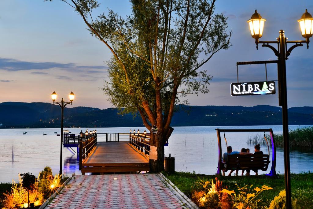 萨潘贾Nibras Villa Resort Hotel的坐在湖岸边的长凳上的人