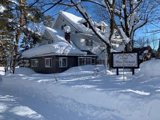 白马村Lodge Blue Mount Hakuba的雪覆盖的房子,前面有标志