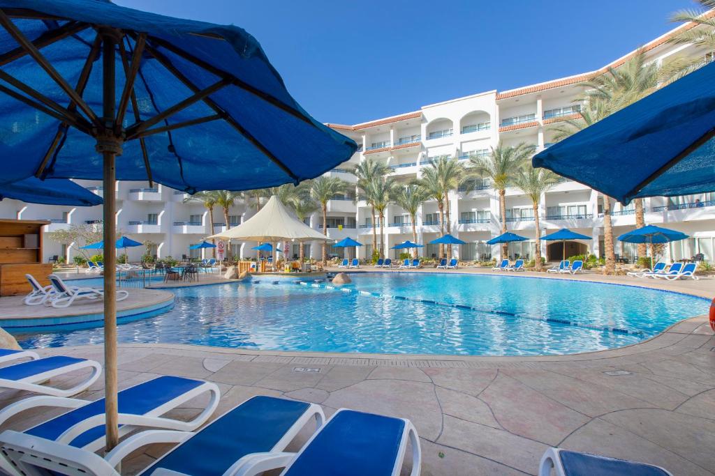 沙姆沙伊赫Naama Bay Hotel & Resort的度假村的游泳池,配有椅子和遮阳伞