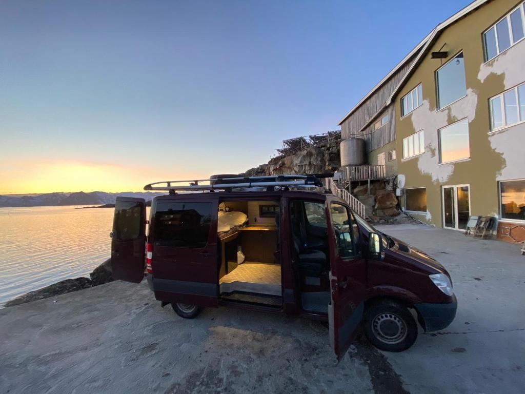 莱克内斯Campervan in the Lofoten Islands的停在水边的建筑物旁边的小货车