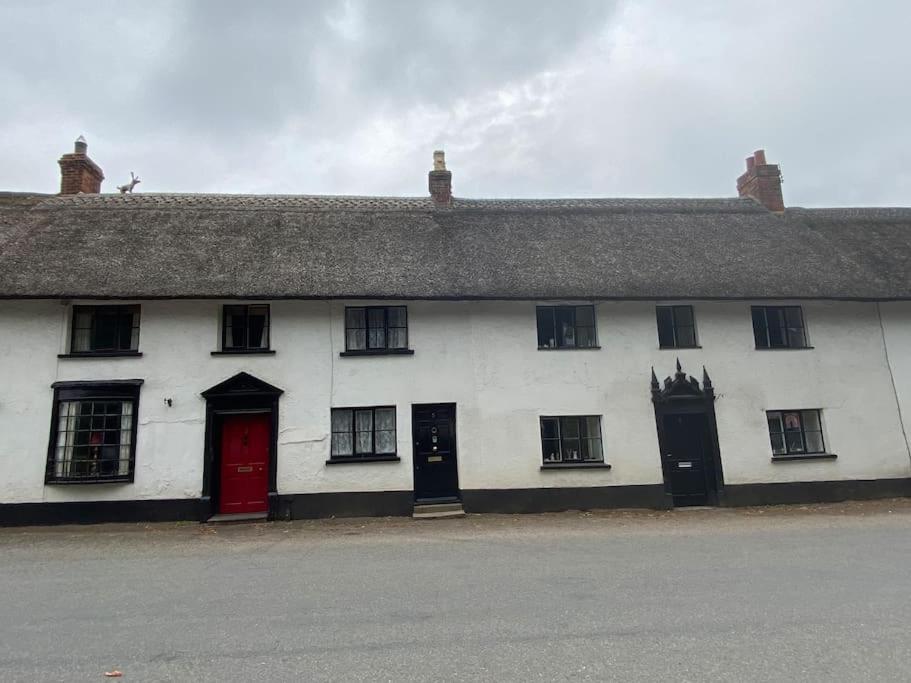 OttertonThatched Cottage, beautiful village near the sea的白色的建筑,设有黑窗和红色的门