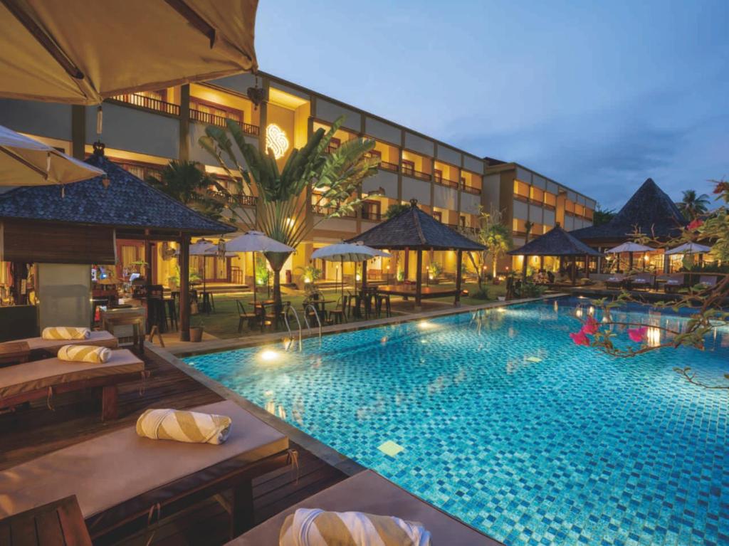 龙目岛库塔Sima Hotel Kuta Lombok的一个带桌子和遮阳伞的酒店游泳池