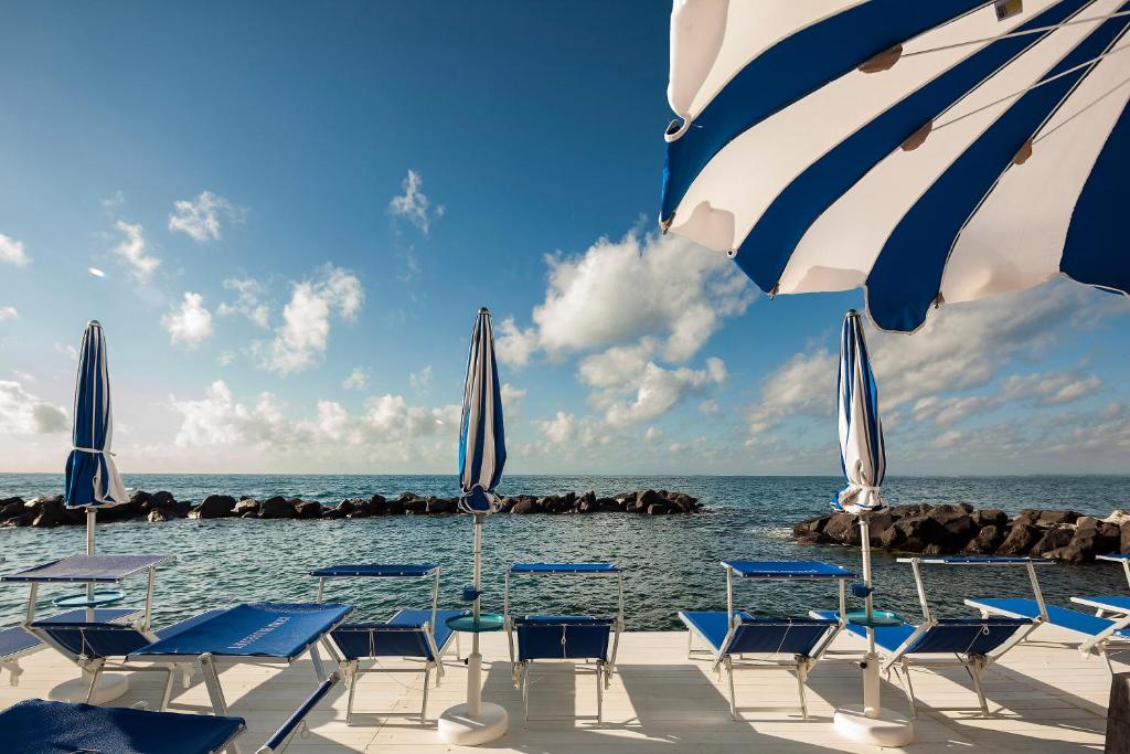 伊斯基亚伊斯基亚蓝光度假酒店的海滩上的一组椅子和遮阳伞