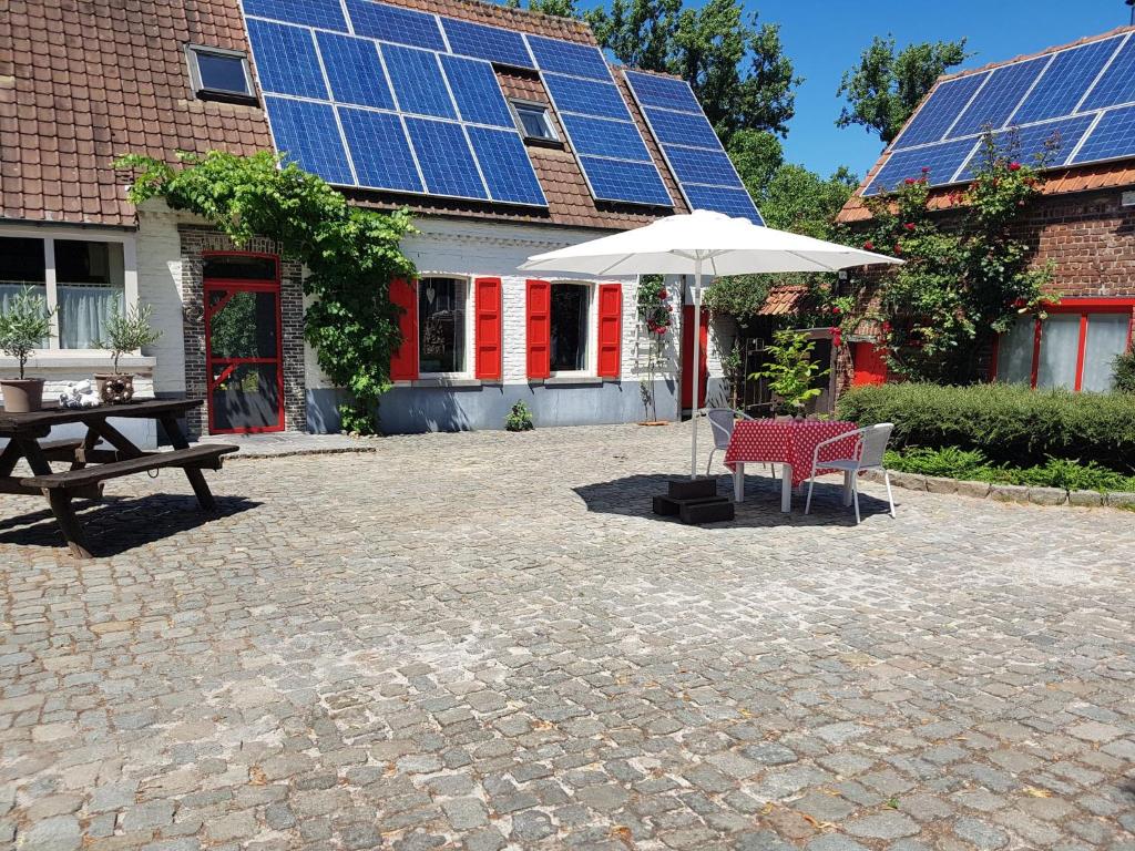 HorebekeB&B Adem的一个带桌子和遮阳伞的庭院和一座带太阳能电池板的建筑