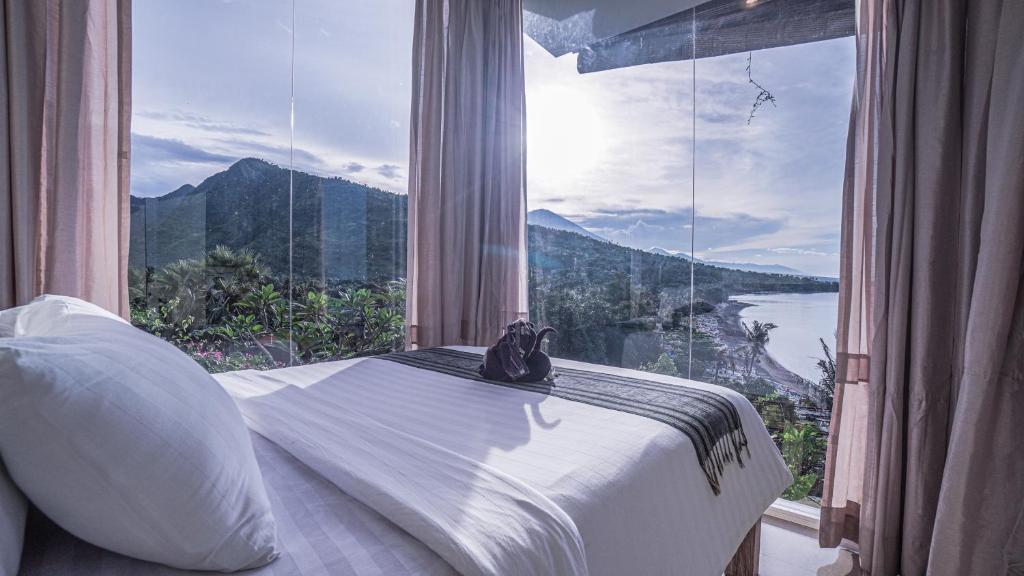 艾湄湾Waenis Sunset View Hotel and Restaurant, Amed, Bali的一张位于带大窗户的房间内的床铺