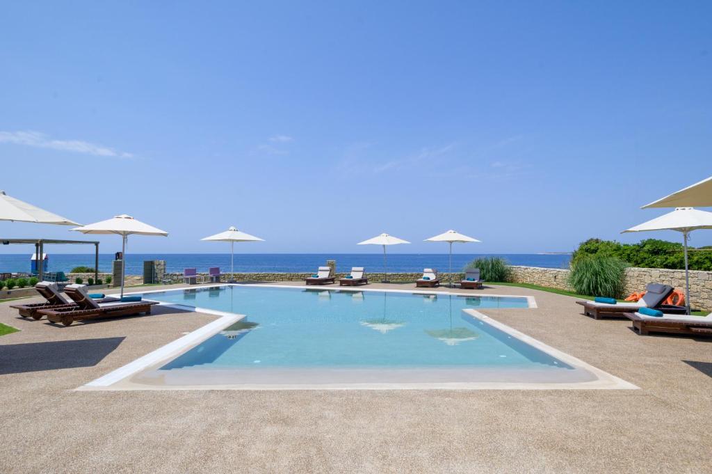 马拉松波利斯Callisto Seaside Homes & Suites的毗邻大海的带椅子和遮阳伞的游泳池