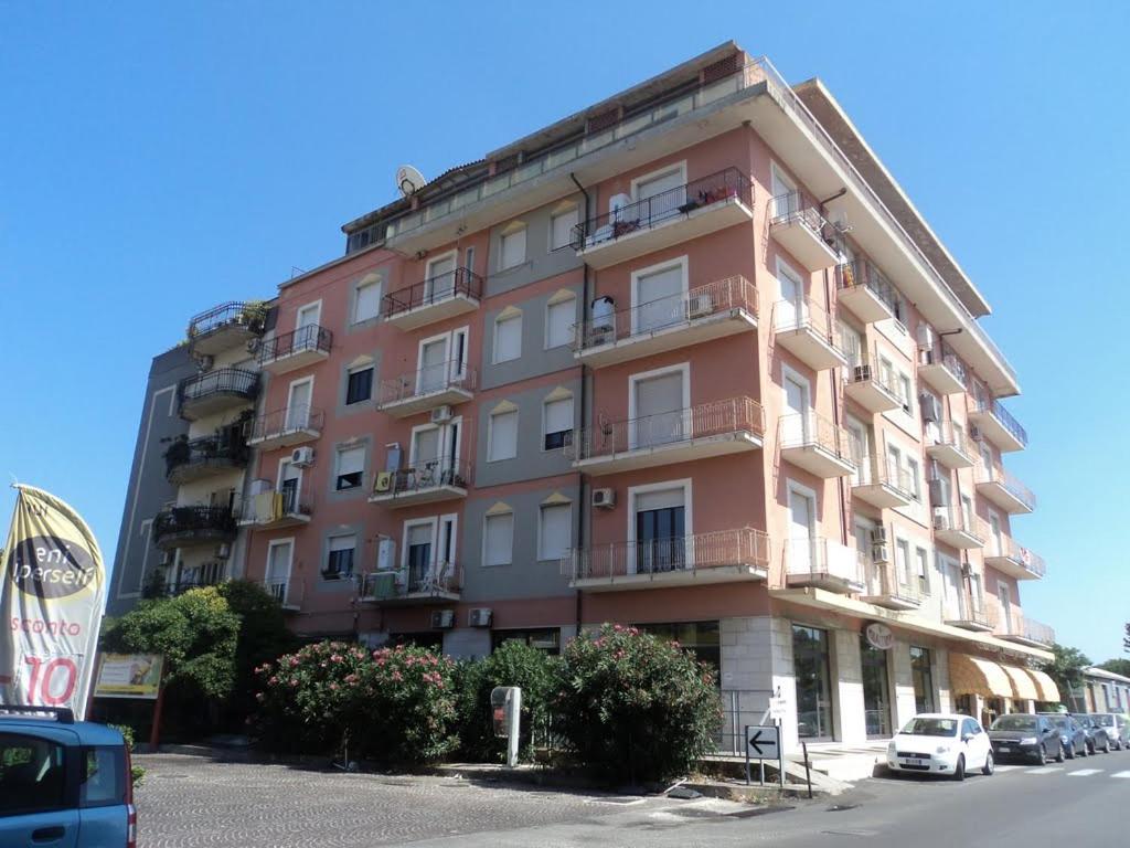 索威拉托玛里纳Corso Umberto Apartment的一座大型粉红色建筑,前面有汽车停放