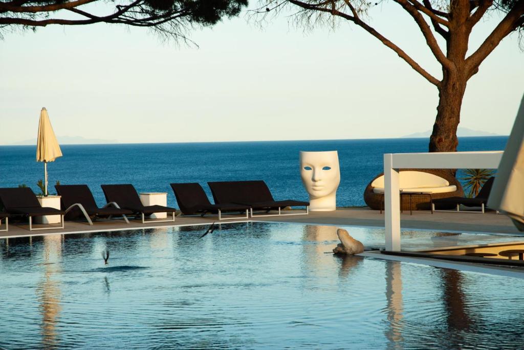 阿祖罗港Resort Capo Bianco的一个带椅子的游泳池,背景是大海