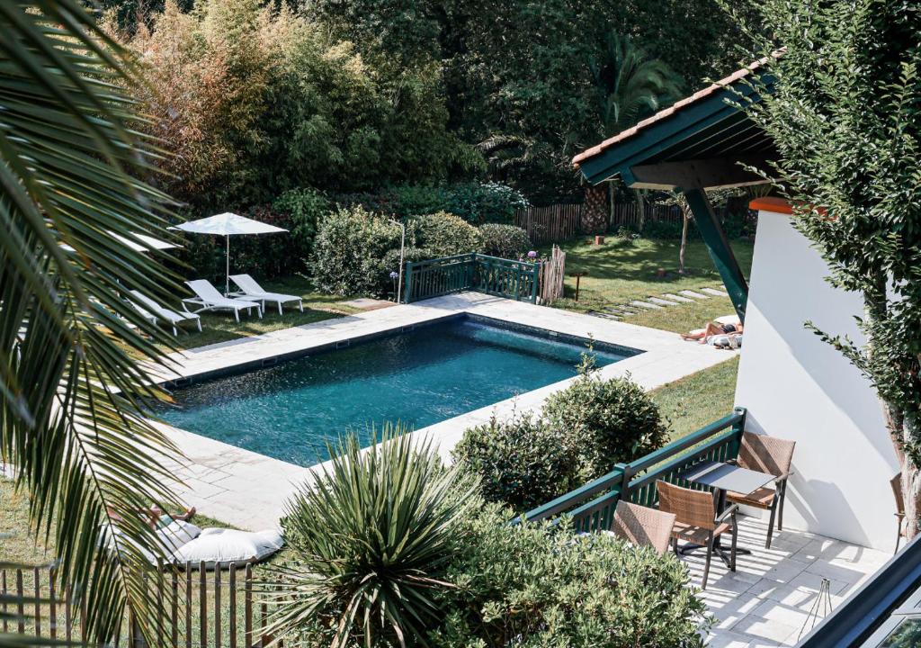 比达尔Hôtel Les Frères Ibarboure的庭院内的游泳池,配有两把椅子和一把遮阳伞