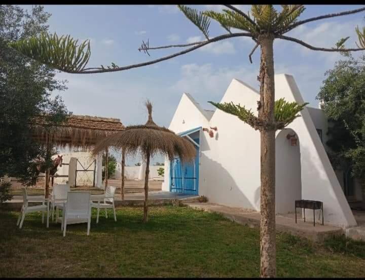乌姆苏克Nouveau Bungalow Djerba的一个带椅子和遮阳伞的庭院和一座建筑