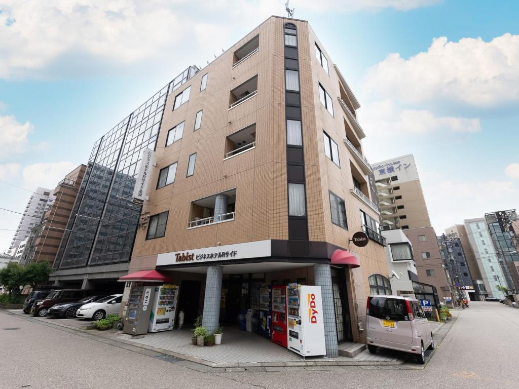 金泽Tabist Business Hotel R Side Kanazawa的一座高大的建筑,前面有一辆货车