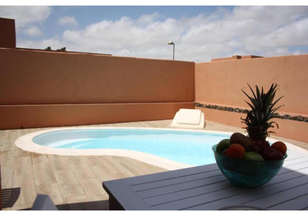 拉奥利瓦Anahi Homes Corralejo - Villa Drago 12的坐在游泳池旁的桌子上,放上一碗水果