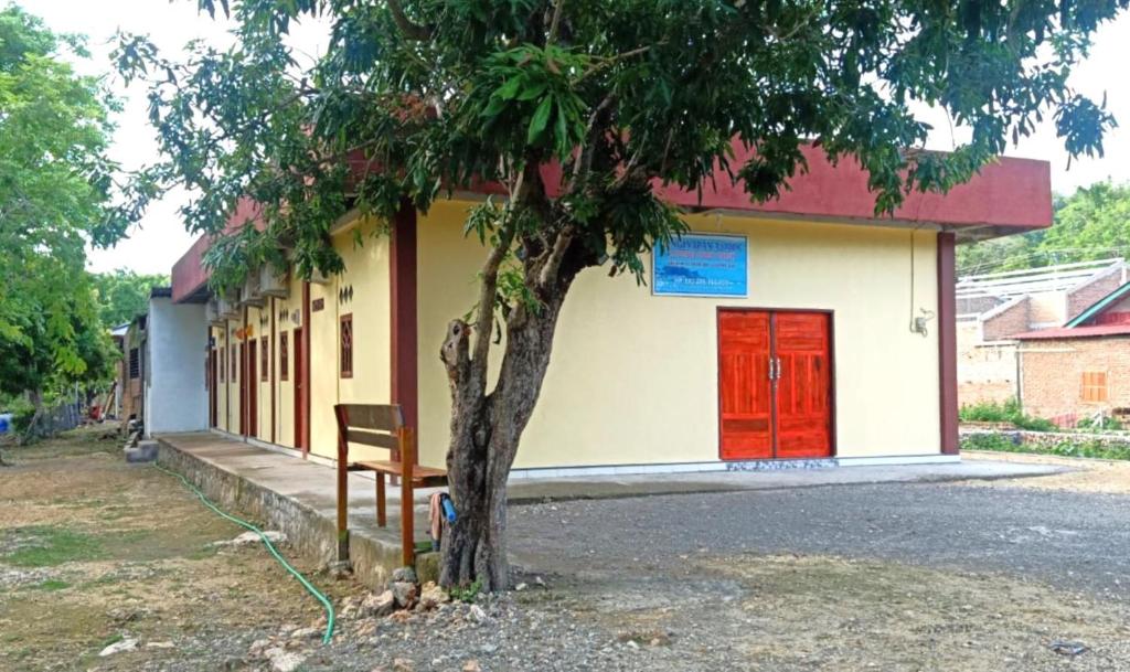 比拉Penginapan asidik的树旁有红色门和长凳的建筑