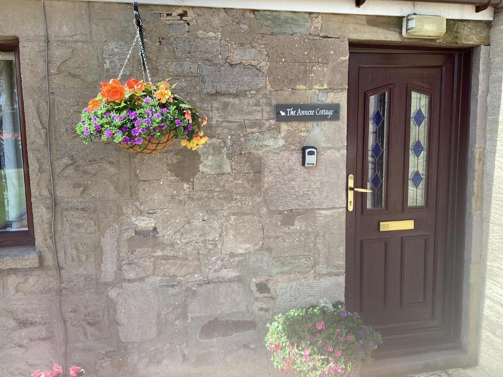拉纳克The Annexe Cottage at Newhouse Farm的石头建筑的一扇门,里面装着一篮花
