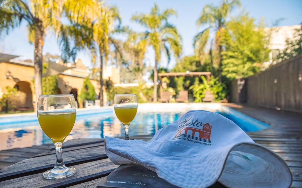 科隆Hacienda Don Justo Hotel Boutique Spa的两杯葡萄酒和一顶帽子在游泳池畔的桌子上
