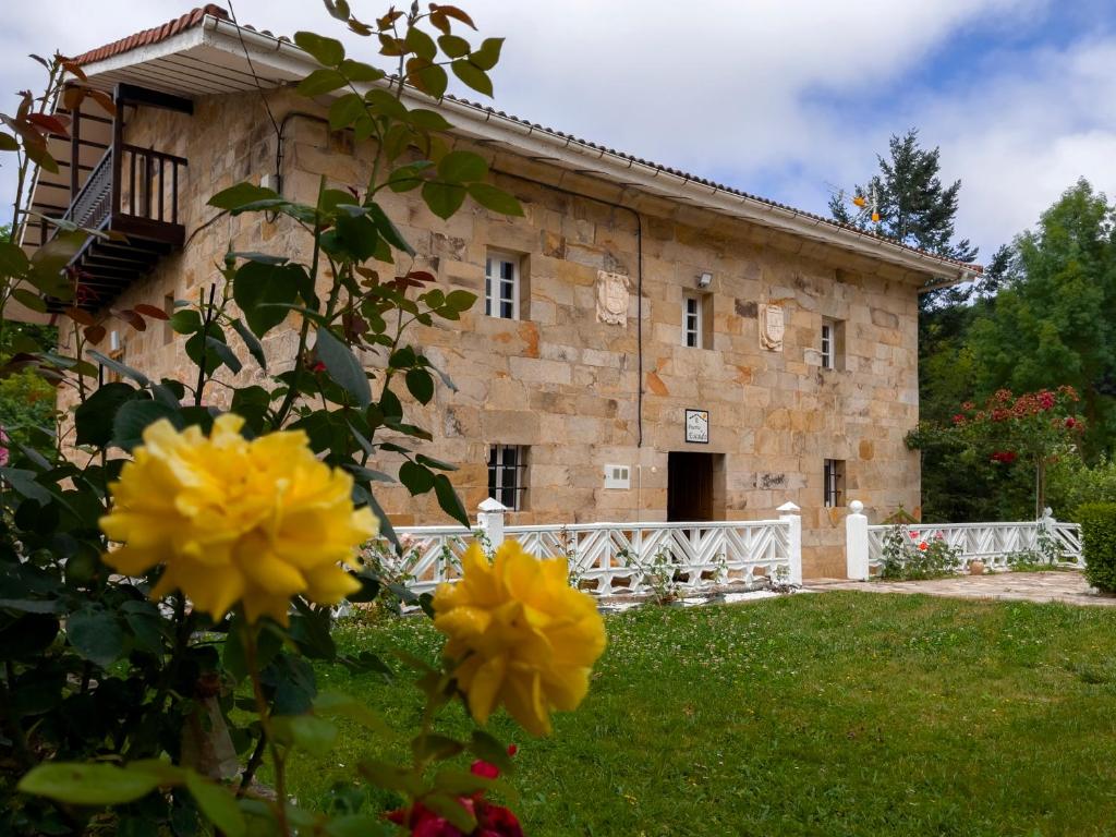 Cilleruelo de BezanaCasa Rural Puerto del Escudo的一座古老的石头建筑,前面有黄色的花朵