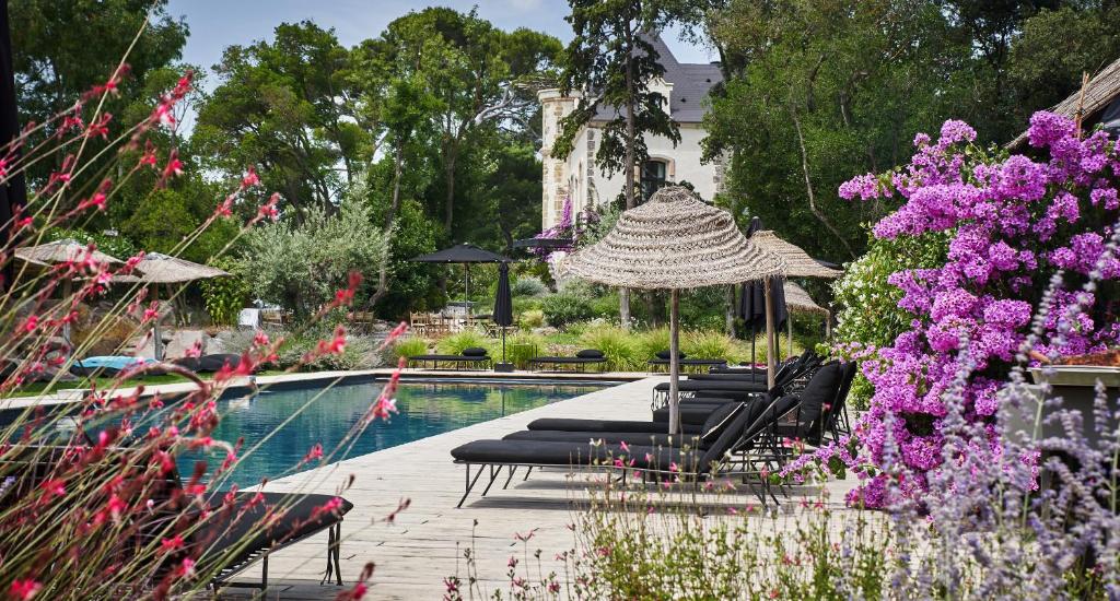 马瑟伊兰Domaine Tarbouriech, Hôtel & Spa的游泳池配有椅子、遮阳伞和紫色鲜花