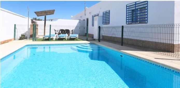 加的斯Casa Enrique的一座蓝色游泳池,旁边是一座建筑,配有两把椅子