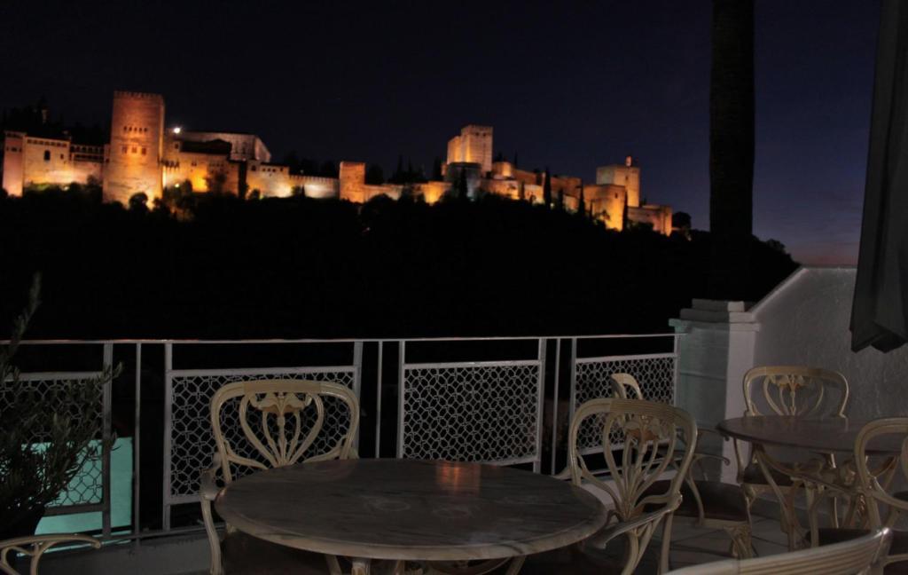 格拉纳达Suite Comares的阳台上的桌椅,晚上有城堡