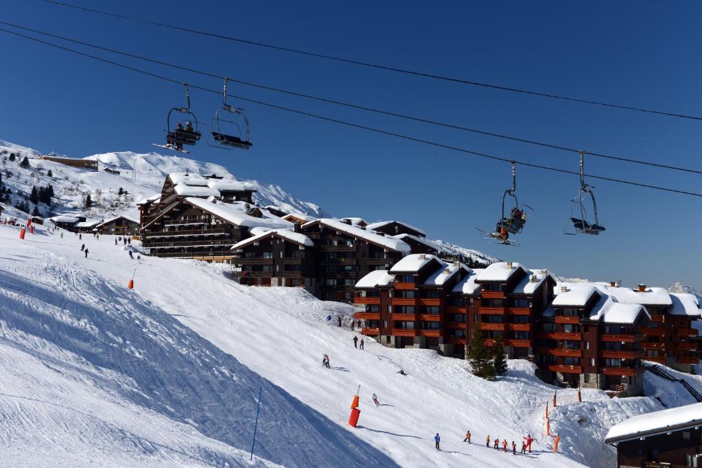 美贝尔Résidence Odalys Le Hameau du Mottaret的滑雪缆车,人们在雪覆盖的斜坡上滑雪