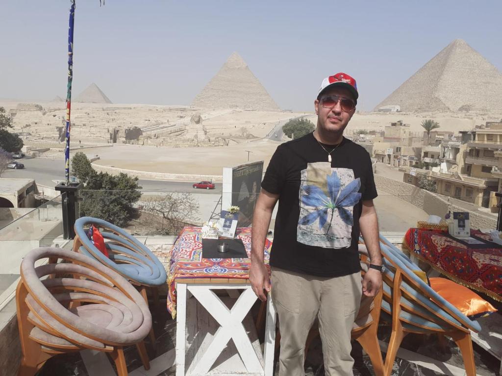 开罗Kenzy guest house的站在一个金字塔背景的阳台上的人