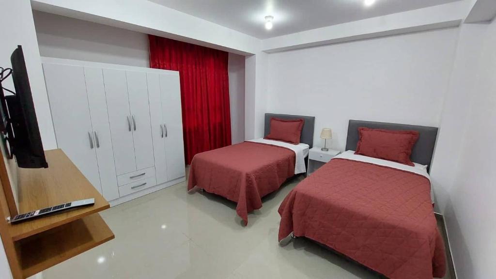 瓦努科Departamentos amoblados en Huánuco的一间卧室配有两张带红色床单的床和电视。