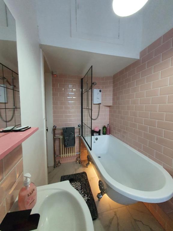 爱丁堡The Flat with the Pink Door的浴室设有粉红色瓷砖,配有大型白色浴缸。