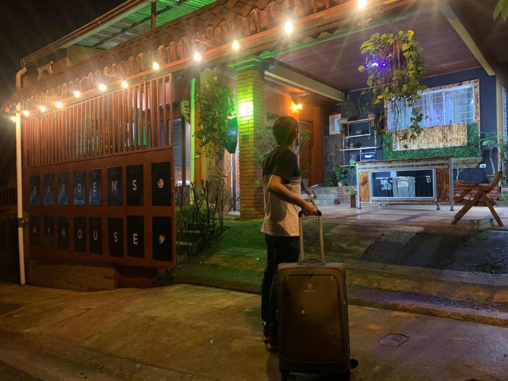 阿拉胡埃拉Gardens House, Airport Juan Santamaría, Alajuela, San José的站在大楼前,手提箱的人