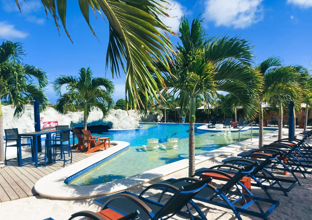 威廉斯塔德The Ritz Hostel的一个带椅子和桌子的度假村游泳池,并种植了棕榈树
