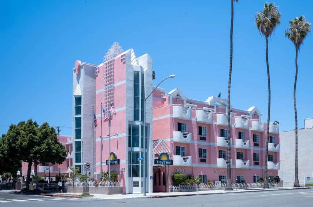 洛杉矶Days Inn by Wyndham Santa Monica的棕榈树街道上的粉红色建筑