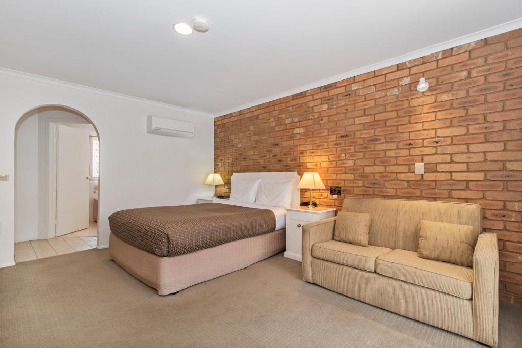 本迪戈黄金广场汽车旅馆的一间卧室配有一张床、一把椅子和砖墙