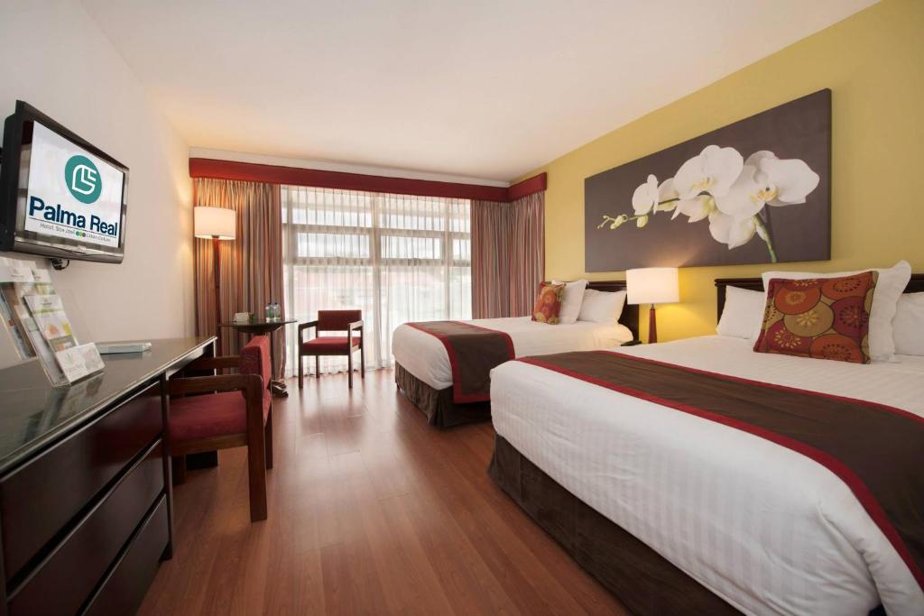 圣何塞Hotel Palma Real的酒店客房设有两张床和一台平面电视。