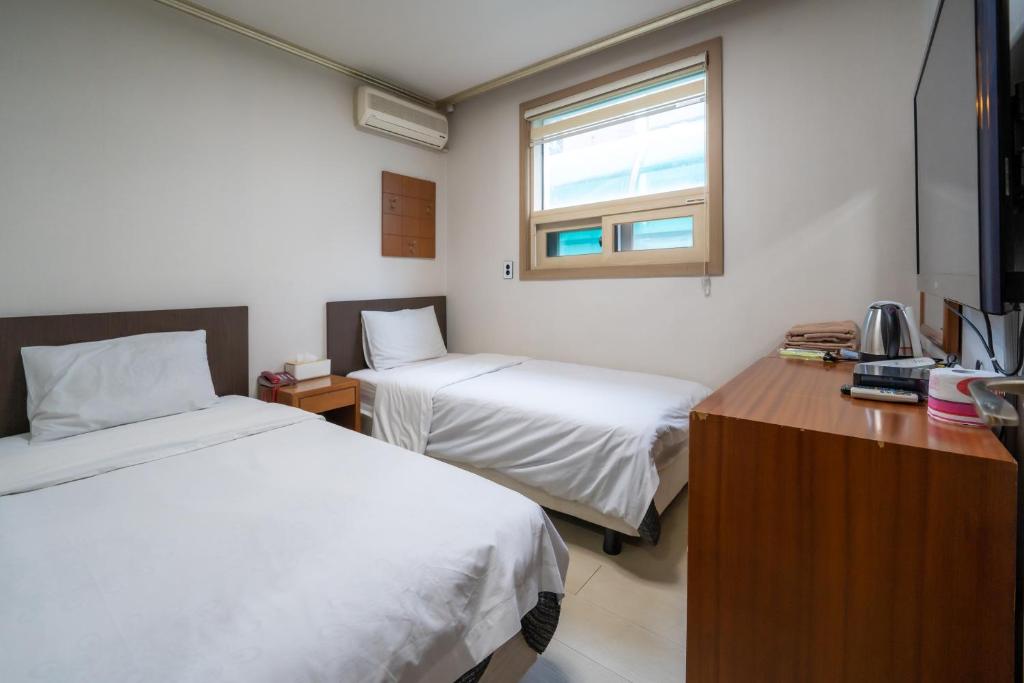 首尔Amiga Inn Seoul Hotel的客房设有两张床、一张桌子和一个窗户。