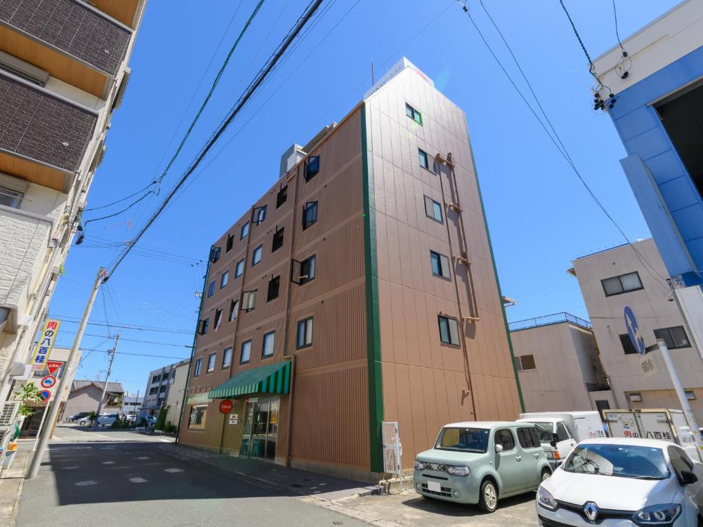 磐田市Tabist IWATA Station Hotel的一座高大的建筑,前面有汽车停放