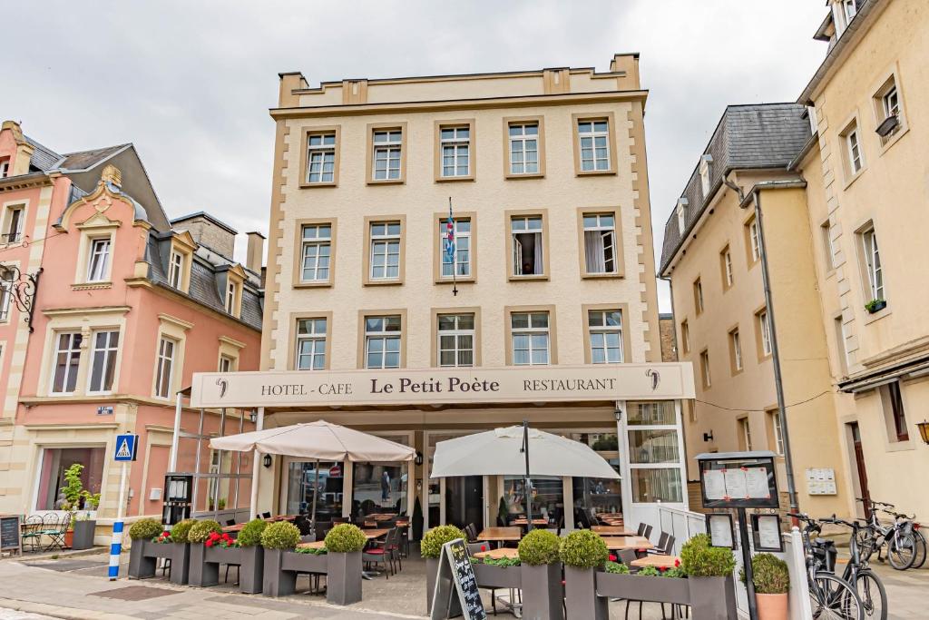 埃希特纳赫Hôtel Le Petit Poète的前面有桌子和伞的建筑