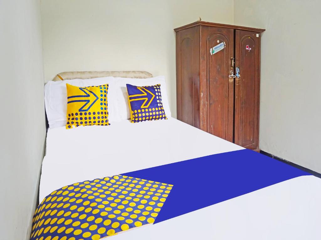 玛琅OYO LIFE 91551 Gwen Syariah Homestay的一张带黄色和蓝色枕头的床和木制橱柜