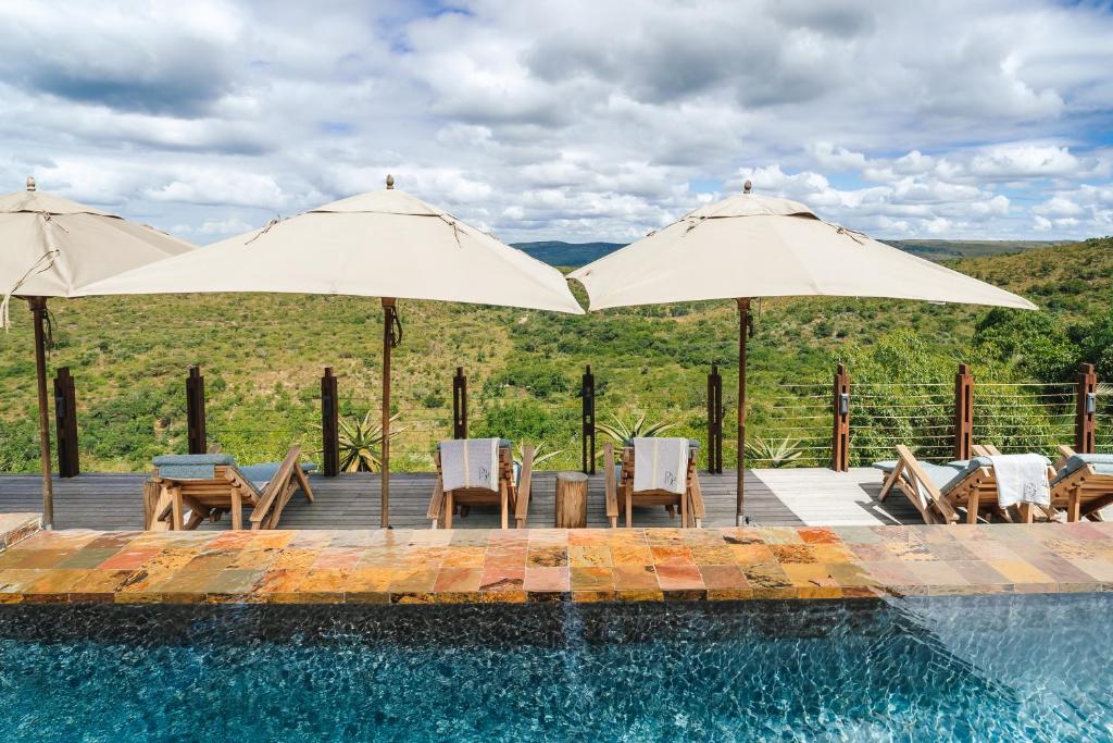 KwaNompondo犀牛岭野生山林小屋的游泳池配有两把遮阳伞和椅子以及桌椅