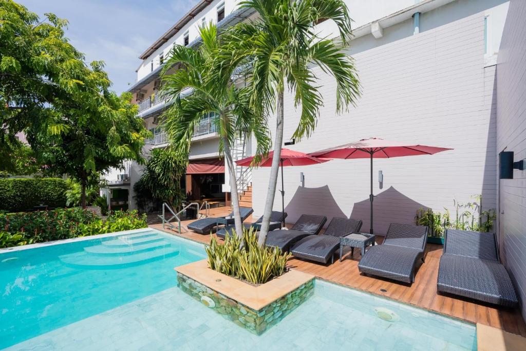 华欣Anchan Hotel & Spa的一座带椅子和遮阳伞的游泳池位于一座建筑旁边