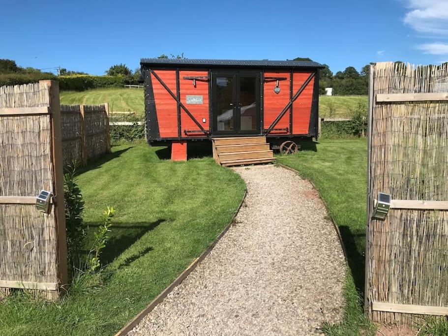 Clodockunique sheperds hut ensuite & kitchenette的两个围栏之间的一个田野上的一个小红色小屋