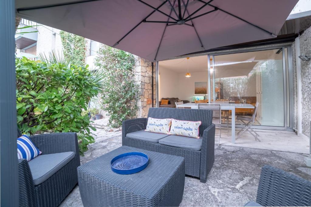 戛纳VILLA L'OASIS - à 80 m du bord de mer et plage的庭院配有椅子、遮阳伞和桌子。