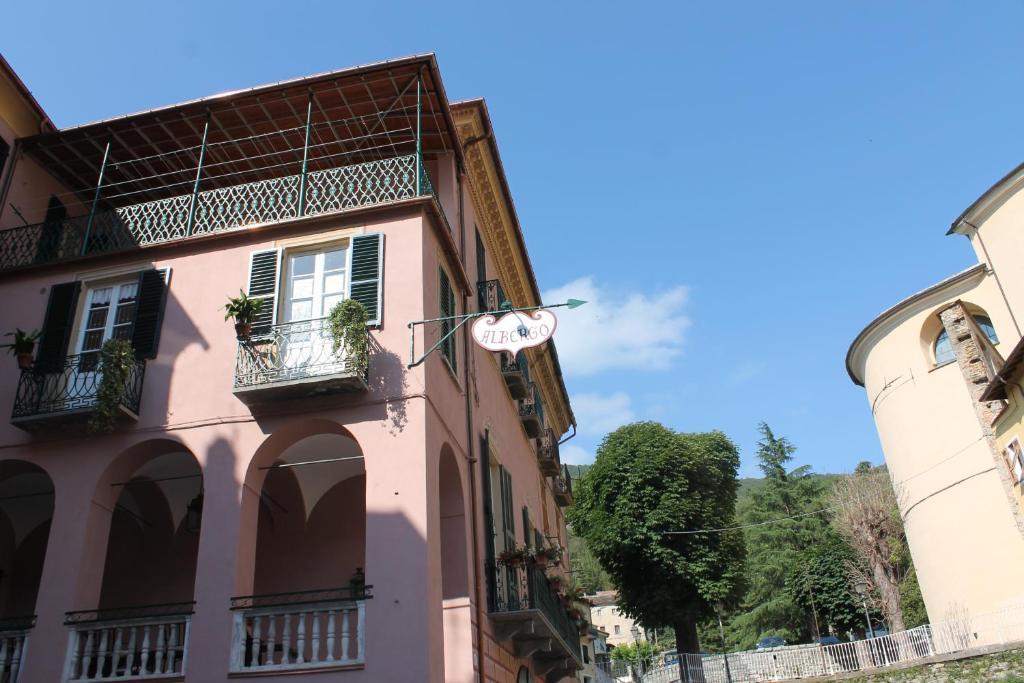 Pieve di TecoAlbergo Dell'Angelo的粉红色的建筑,设有窗户和阳台,位于街道上