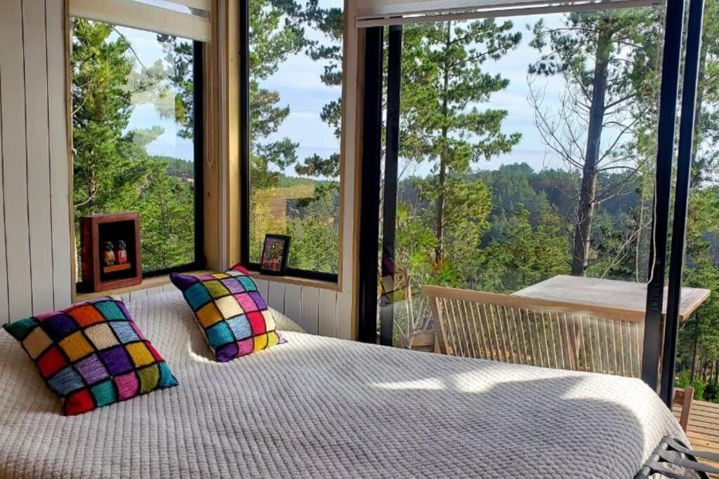 维丘肯Tinyhouse Boyeruca Lodge. Maravillosas vistas de Bosque, Mar y Cielo的卧室设有一张位于大窗户前的床铺。