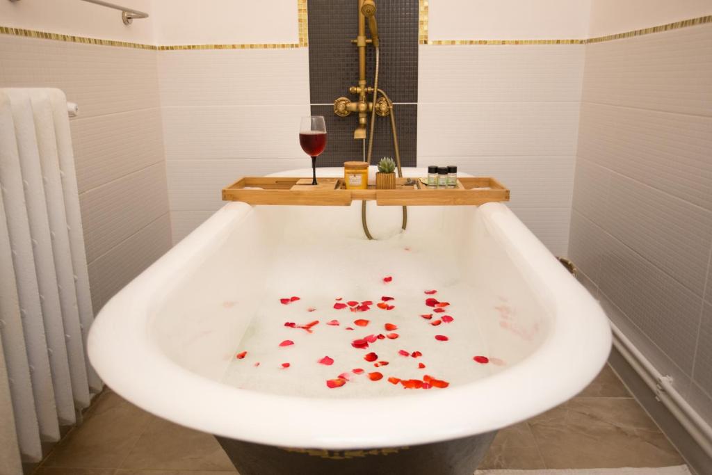 锡吉什瓦拉Joseph Hayn Apartments的装满红色花瓣的浴缸以及一杯葡萄酒