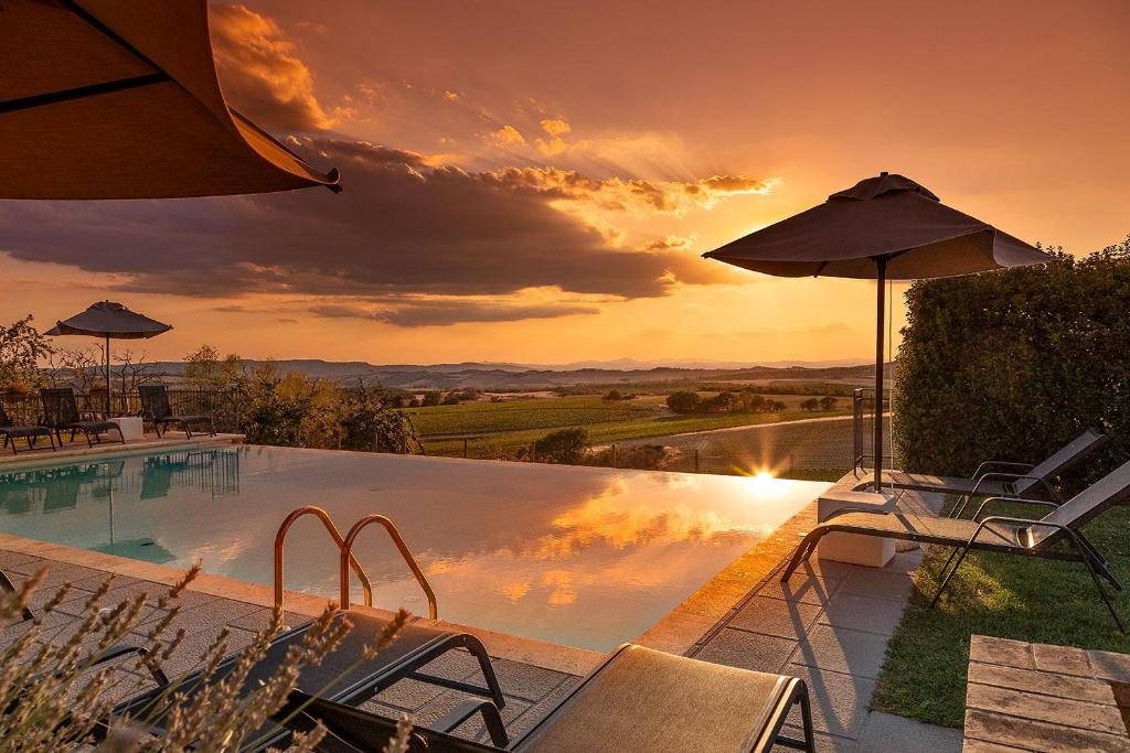 皮恩扎Palazzo Massaini - La Pieve的一个带椅子和遮阳伞的游泳池,享有日落美景